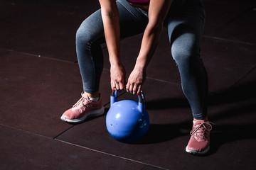 Naklejka premium Young sweaty strong muscular fit girl hands holding heavy kettlebell on the floor concentrating and preparing for hardcore cross swing workout training in the gym selective focus