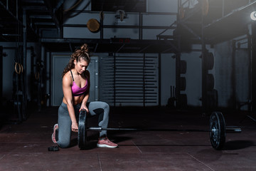 Young strong muscular fit girl with big muscles preparing for hard strength weightlifing or dead lift cross workout training with barbell weights in the gym real people exercising