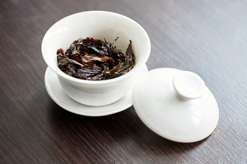 Chinese porcelain gaiwan for tea ceremony or gong fu cha or kung fu tea for brewing oolong, on wooden table or chaban with wet tea leaves close up.