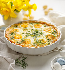 Easter tart quiche with eggs and green peas in casserole dish on a white table
