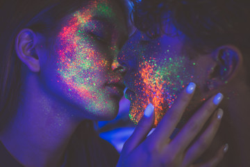 Couple kissing in the disco club with fluorescent paintings on the faces