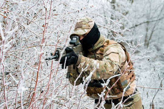 Airsoft man in camouflage uniform and machinegun with optical sight. Soldier in the winter forest. Horizontal photo side view.