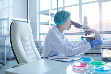 Horizontal medium side view portrait of young Asian female scientist analyzing liquid content using microscope, copy space