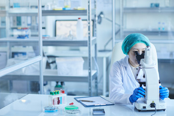 Horizontal shot of chemical industry worker sitting alone in modern laboratory using microscope, copy space