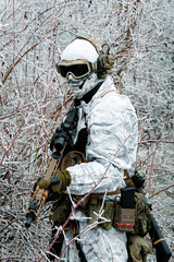Military man in white camouflage uniform with machinegun. Soldier in the winter forest territory...