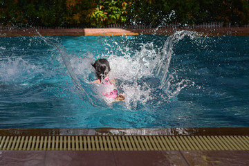 Little girl jumping in pool on a summer day, huge splash.