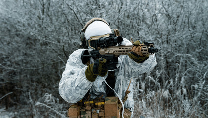 Fototapeta premium Closeup military man in white camouflage uniform with machinegun. Soldier aims of the machinegun