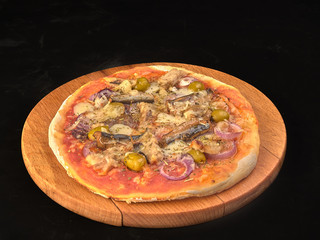 Pizza with sardines, tomatoes and olives on a thin dough.On black background