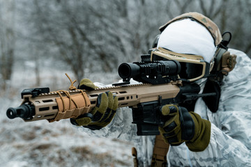 Closeup military man in white camouflage uniform with machinegun. Soldier aims of the machinegun