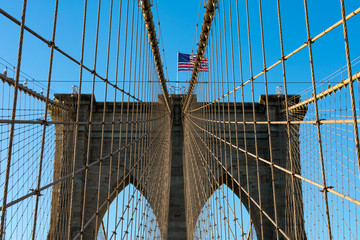 Obraz premium Arches on the Brooklyn Bridge with an American Flag in New York City and a Blue Sky