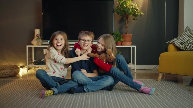 Happy lovely moment of triplets little kids hugging and kissing in cozy living room indoor, pretty casual Caucasian children brother and sisters family with horse toy cute moment together at home