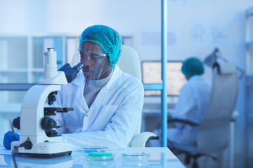 Horizontal shot of African American male medical scientist working in modern laboratory using microscope and making notes, copy space