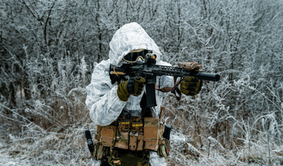 Closeup military man in white camouflage uniform with hood and aims of the machinegun. Horizontal photo side view.