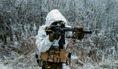 Closeup military man in white camouflage uniform with hood and aims of the machinegun. Horizontal...