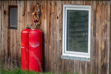 outside wall of a small wooden house are two big red gas bottles for heating