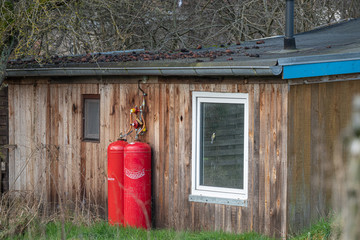 outside wall of a small wooden house are two big red gas bottles for heating