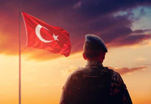 Turkish Soldier is stand and salute front of Turkish Flag on his watch duty.
