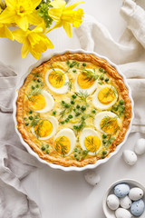Easter tart quiche with eggs and green peas in casserole dish on a white table, top view