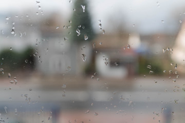 Widok na ulicę przez okno pokryte kroplami deszczu.