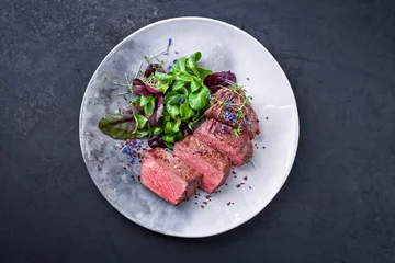 Foto op Aluminium Barbecue dry aged wagyu roast beef natural sliced and offered with lettuce and herbs as top view on a modern design plate with copy space © HLPhoto