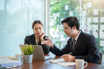 Two young asia business colleagues working together on new project with a laptop computer in the office.