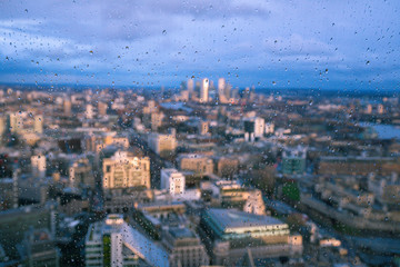 Obraz premium Raindrops on a window pane of glass with blurred background of River Thames and City of London Canary Wharf financial district