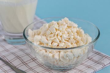 Fresh cottage cheese in a transparent bowl with a spoon with a glass of kefir on a blue background. Fermented foods. Good bacteria for health.