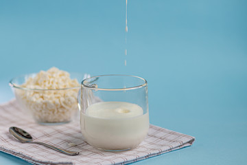 Fresh cottage cheese in a transparent bowl with a spoon and a glass in which a stream of kefir is...