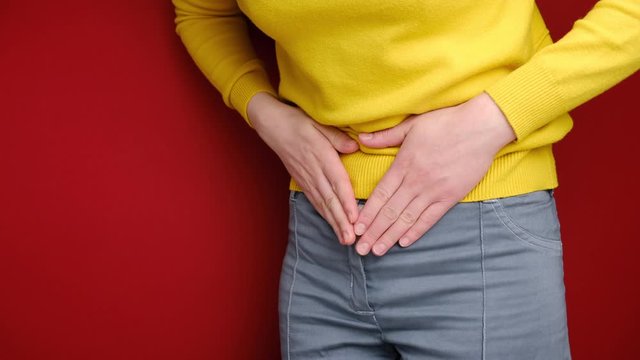 Close up of sick young woman stand hold embracing belly suffer from stomach ache feel discomfort or indigestion, twinges of pain caused by menstrual period, wears sweater, isolated on red background