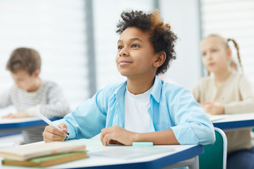 Horizontal potrait of young African American boy sitting at school desk attentively listening to...