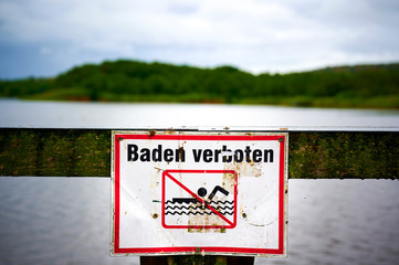 Sign with a pictogram that prohibits swimming. The text means bathing prohibited in German.