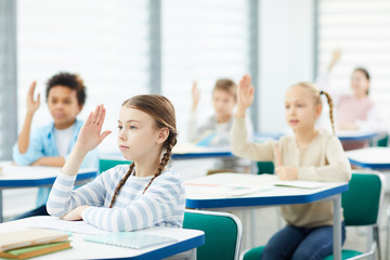 Active young boys and girls sitting at school desks raising their hands in class, horizontal shot, copy space