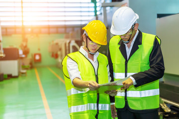 Businessmen or male engineers and female engineers are working in industrial plants that have machines and injection molds, with tablets used to control technology.