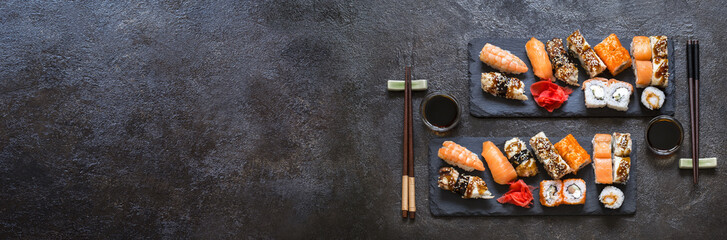 sushi rolls with rice and fish, soy sauce on a dark stone background