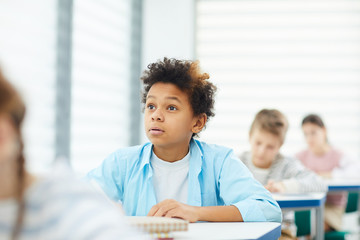 Curious teen boy with eyes wide open sitting at school desk listening to his teacher, horizontal portrait, copy space
