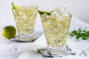Glasses are filled with ice and cold green tea. Garnished with lime slices and a sprig of mint. On a light background.