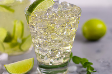 Glasses are filled with ice and cold green tea. Garnished with lime slices and a sprig of mint. On a light background.