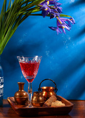 still-life. Red drink in a crystal glass. Copper dishes. On a blue background in the morning sun