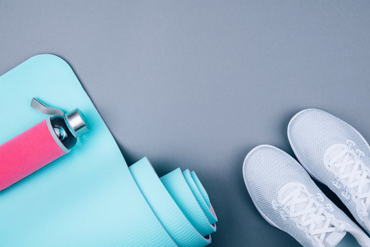 White sport shoes sneakers, blue yoga mat and glass water bottle on grey background.