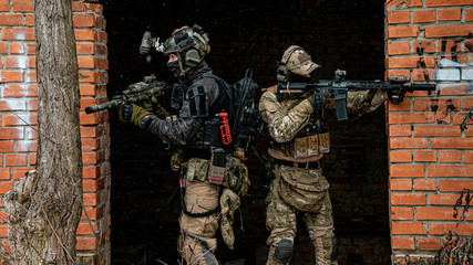 Two men in camouflage cloth and black uniform with machineguns stand back to back. Soldiers with...