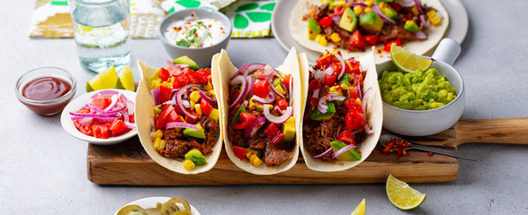 Taco with meat and vegetables on cutting board. Grey background. Close up.