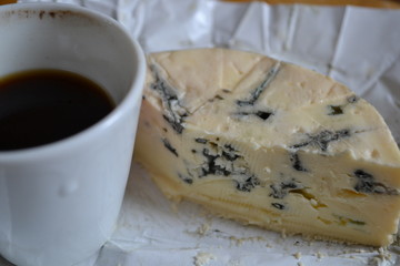 A cup of coffee and a piece of blue cheese.