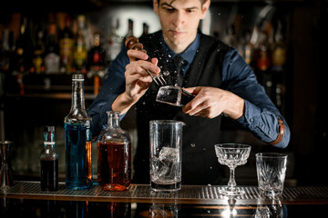 Young bartender professionally splits pieces of ice to make a cocktail.