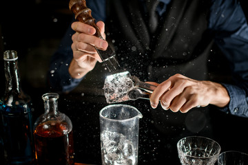 Barman professionally breaks ice and small fragments fly around.