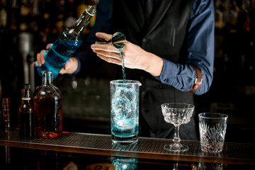 Bartender add necessary ingredient to glass with cocktail.