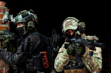 Fototapeta premium Closeup two men in camouflage cloth and black uniform with machineguns stand beside brick wall. Soldiers with muchinegun aims aiming