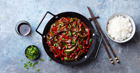 Beef and vegetables stir fry in a pan and rice. Blue stone background. Top view.