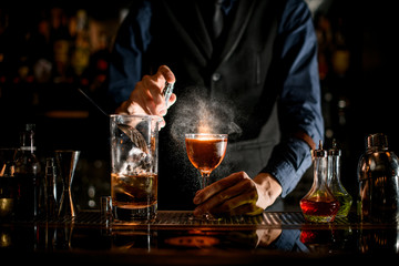 Bartender sprinkles on a glass with a brown alcoholic drink.