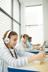 Young students sitting in classroom using modern gadgets during lesson, vertical shot, copy space