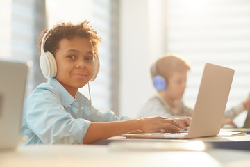 Medium portrait of African American boy wearing headphones using laptop while studying at school, copy space - obrazy, fototapety, plakaty